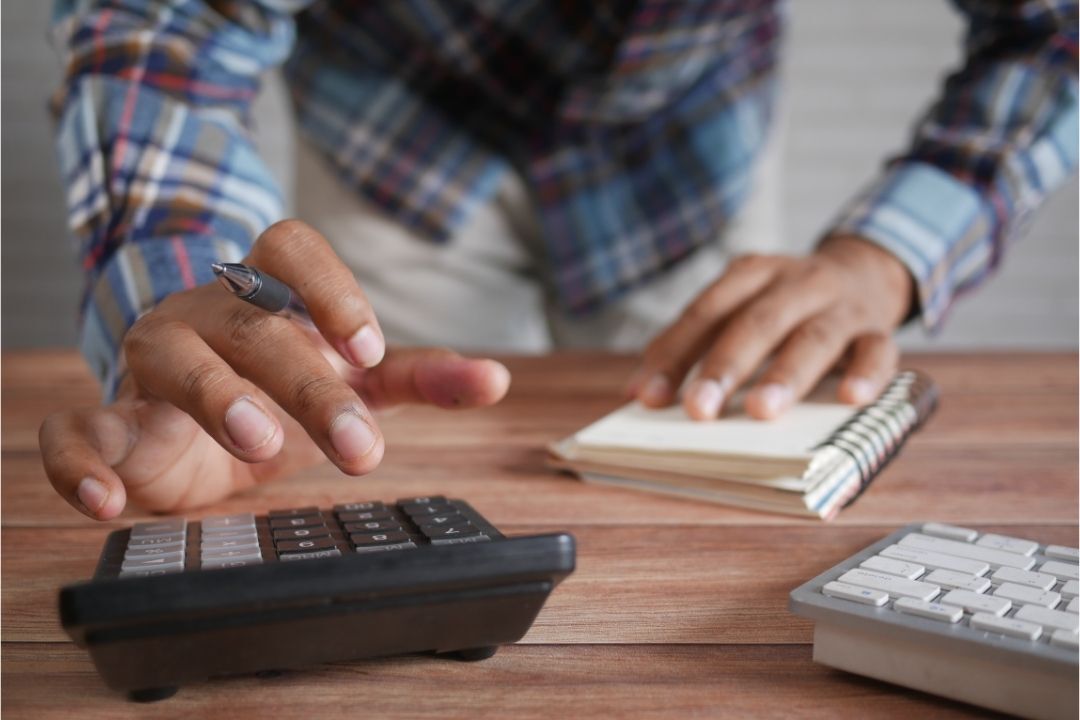 Homem realizando a gestão de custos utilizando uma calculadora e um caderno