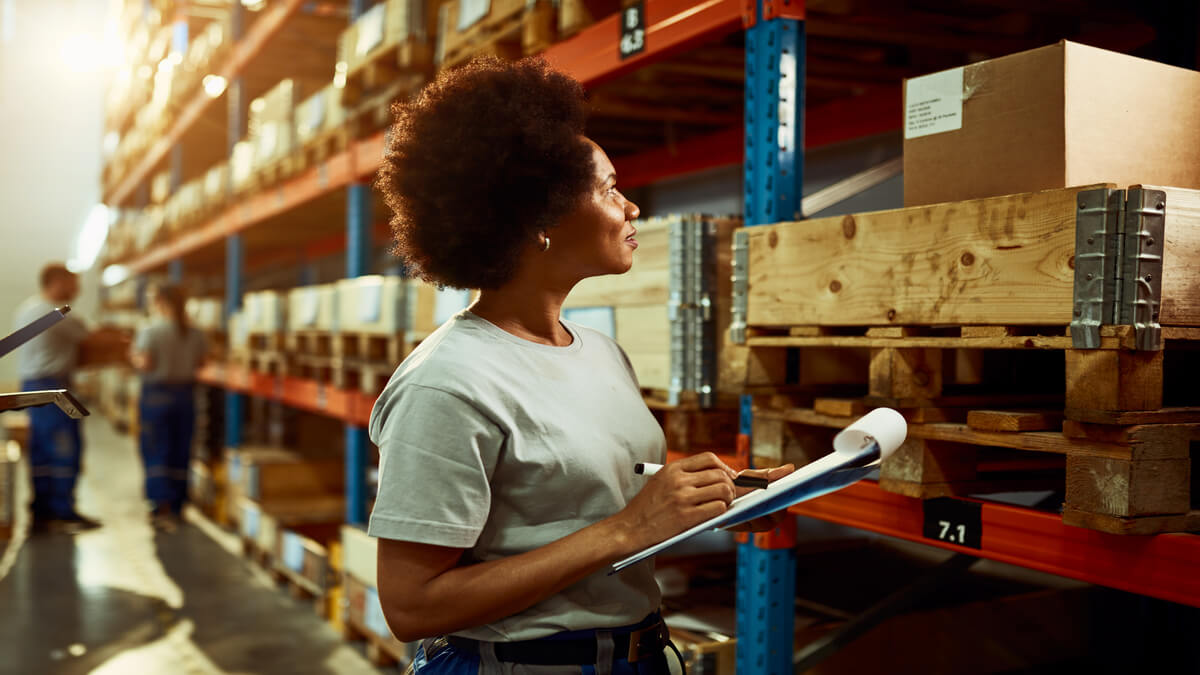 Trabalhadora afro-americana escrevendo lista de inventário enquanto verifica o estoque na sala de armazenamento